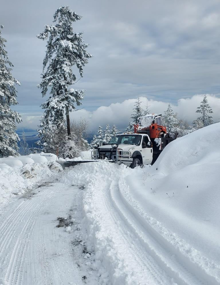 AMROK'S truck plowing snow on a road at the top of a mountain.